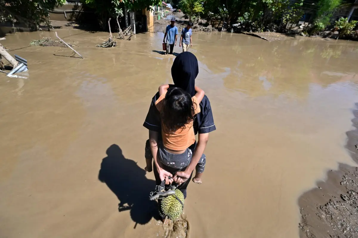 People walk through a flooded area in Meureudu, Pidie Jaya district in Indonesia's Aceh province on November 30, 2025. The death toll from floods that hit Indonesia this week has risen to more than 300 people, according to figures from the disaster agency on November 29. (Photo by CHAIDEER MAHYUDDIN / AFP)