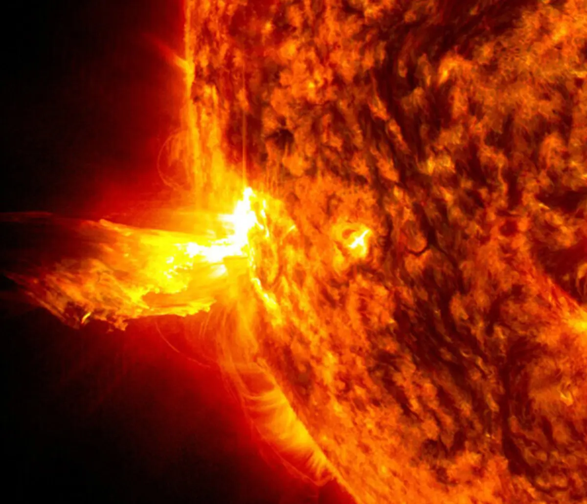 Luz brilhante de uma erupção solar no lado esquerdo do Sol