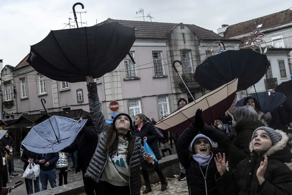 Pessoas recorrem a guarda-chuvas para apanhar doce lançado do alto da capela