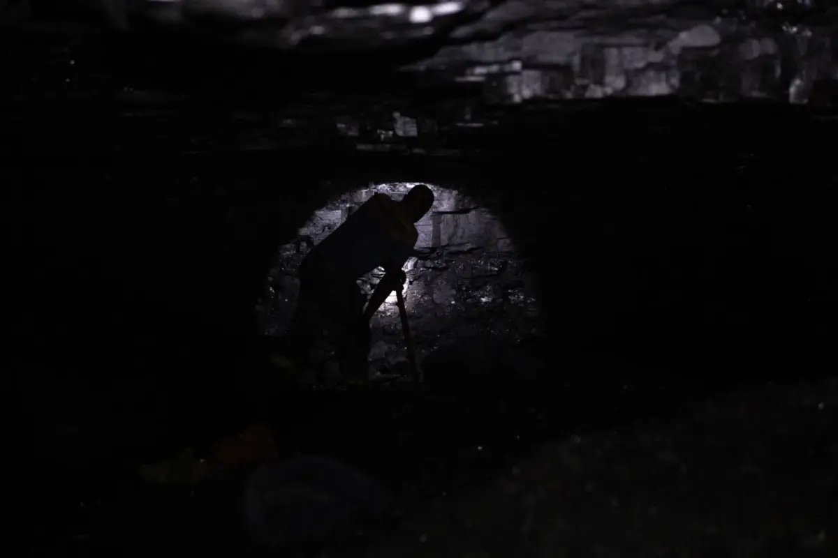 An artisanal miner examines a coal seam inside a tunnel at the Golfview informal coal mine in Ermelo on September 26, 2025. As South Africa slowly begins to move away from coal - spurred by the landmark $8.5 billion Just Energy Transition deal struck at COP26 in 2021 - communities in mining areas that saw little benefit from decades of extraction fear they"ll be left behind once again. Entire communities in Mpumalanga province rely on artisanal and illegal mining in the absence of other economic activities, and many depend on illegally sourced coal for cooking and heating. Yet as the government intensifies its crackdown on illegal mining, locals and experts say that support to help these communities transition remains almost nonexistent. (Photo by EMMANUEL CROSET / AFP)
