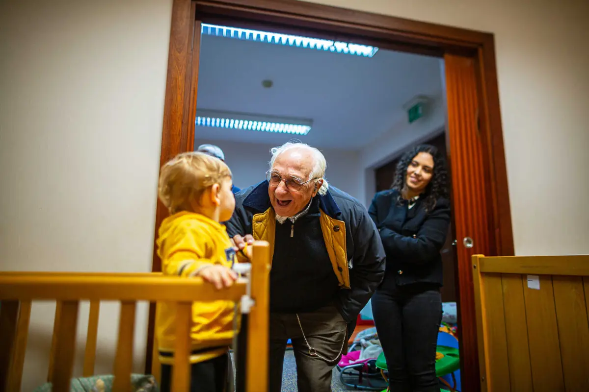Padre Artur Coutinho, responsável do Berço, mima uma das crianças, perante o olhar da nova coordenadora, Beatriz Sousa