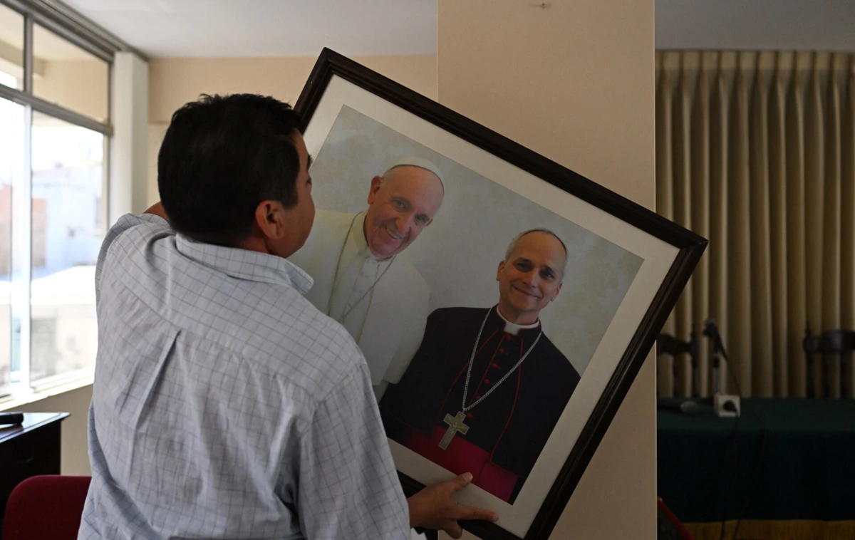 Homem com fotografia do Papa Francisco e do então cardeal Robert Prevost, futuro Leão XIV, na cidade em que o novo Pontífice trabalhou, Chiclayo, no Peru
