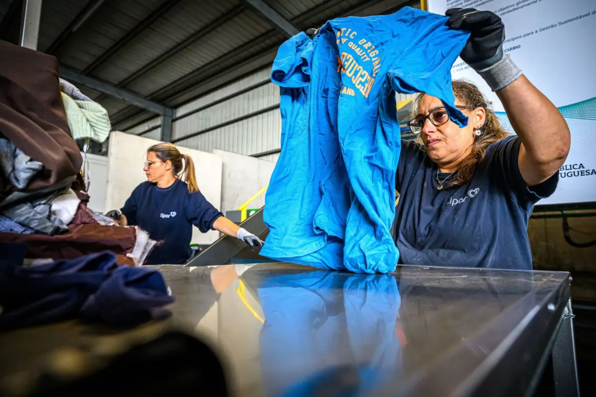 Funcionários colocam roupa em máquina de triagem têxtil