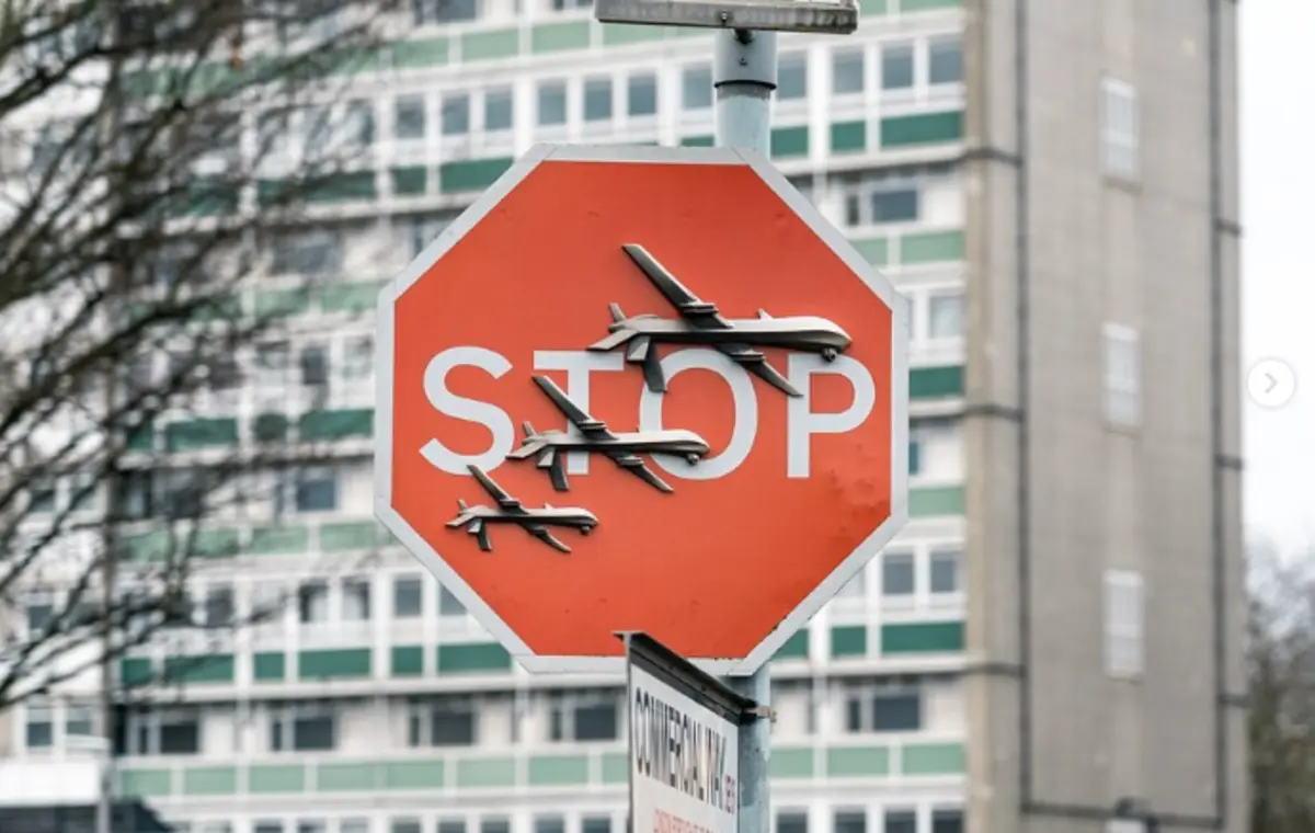 A obra representa três drones de guerra, pintados sobre uma placa de stop