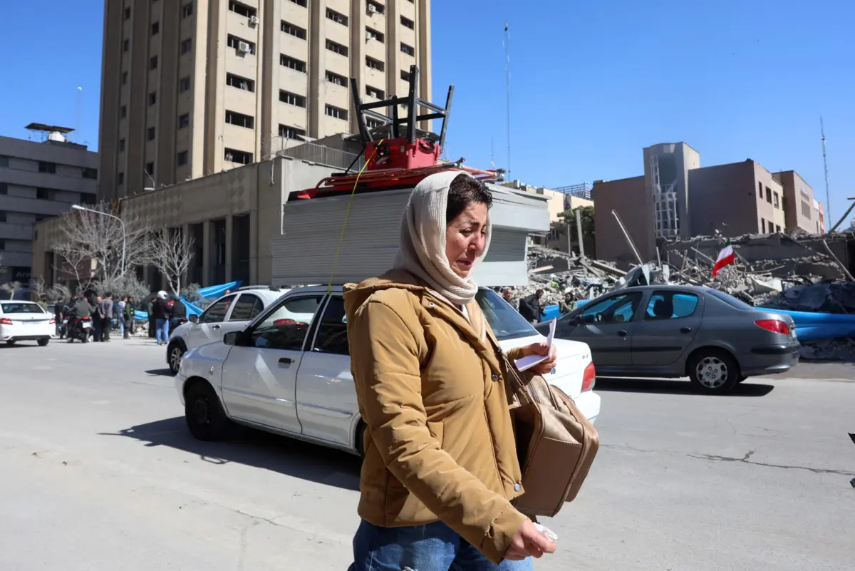 Mulher iraniana desolada com destruição como pano de fundo