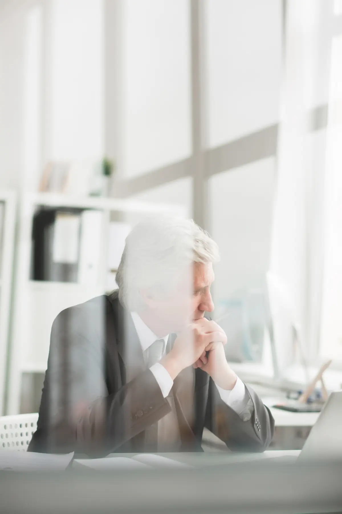 Pensive mature grey-haired businessman sitting by workplace in his office