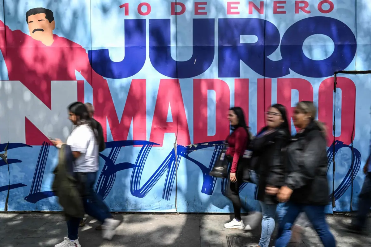 People walk past a mural featuring propaganda in support of Venezuela's President Nicolas Maduro in Caracas on December 17, 2025. Venezuela struck a defiant note on December 17, insisting that its crude oil exports were not impacted by US President Donald Trump's announcement of a potentially crippling blockade. (Photo by Juan BARRETO / AFP)