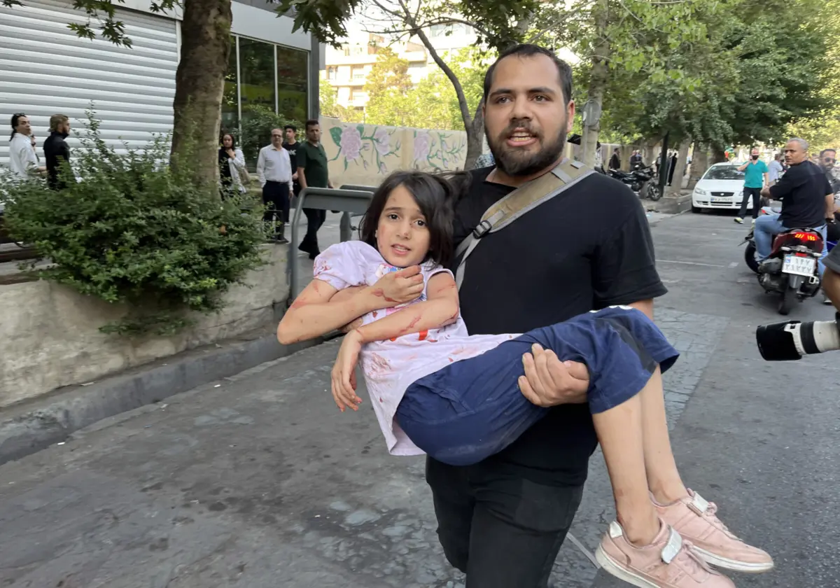 Um homem leva ao colo uma criança ferida, em Teerão